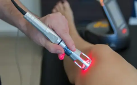Fizjoterapeuta wykonuje laser zabieg rehabilitacyjny na kolanie pacjenta.