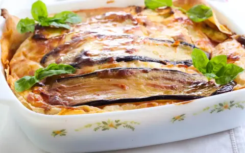 Parmigiana di melanzane napoletana recién horneada, dorada y burbujeante, decorada con hojas de albahaca fresca.