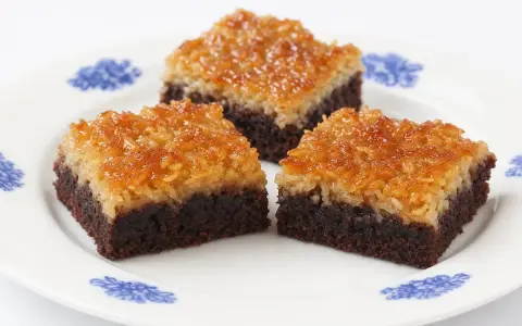 Chokladkakor med kokostosca, perfekta att baka i långpanna. Tre bitar på en vit tallrik med blått mönster.