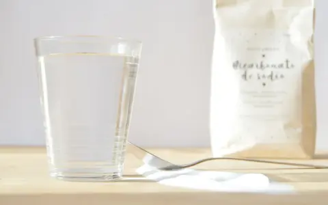 Un vaso de agua, una cuchara con bicarbonato y una bolsa de bicarbonato de sodio. ¡Listo para mezclar con vinagre!