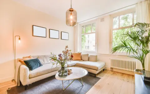 Przytulny salon z sofą w kolorze beżowym, marmurowym stolikiem i bukietem kwiatów.