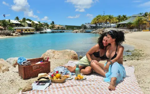 Two women enjoy a picnic on a beach in Curacao, a gay-friendly paradise.