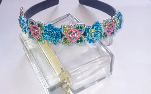 Elegancka opaska z kamieniami w kształcie kwiatów, ozdobiona niebieskimi różami i różowymi detalami, błyszczy na szklanym flakonie.