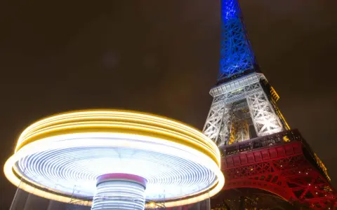 Manège lumineux tournant devant la Tour Eiffel illuminée en bleu, blanc et rouge. Une scène de Paris nocturne, parmi les plus belles photos de nuit.