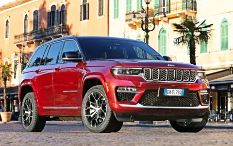 Czerwony Jeep Grand Cherokee zaparkowany na brukowanej ulicy przed budynkami z balkonami.