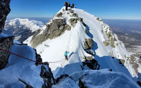 Grupa turystów na ośnieżonym szczycie. Widok na zimowe Tatry dla średniozaawansowanych.
