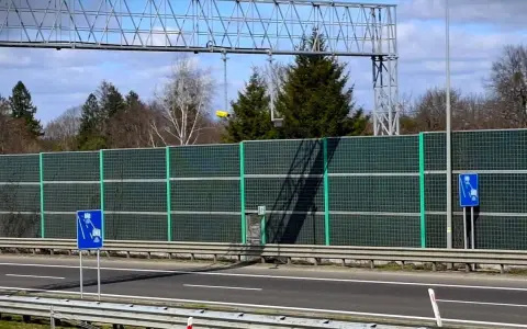 Znak drogowy informujący o odcinkowym pomiarze prędkości na tle ekranów akustycznych i drzew.