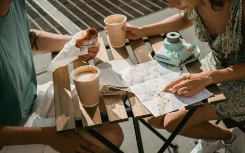 Para planuje podróż, studiując mapę i jedząc croissanty. Na stole kawa i aparat.
