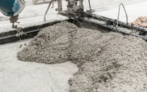 Beton wylewany z betoniarki na podłoże z drobnego kruszywa. Widać formę do wylewania betonu i masę, która tworzy kopiec.