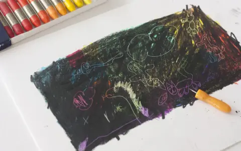 Un niño empieza a dibujar con ceras sobre un papel negro, revelando colores vibrantes y figuras fantásticas.
