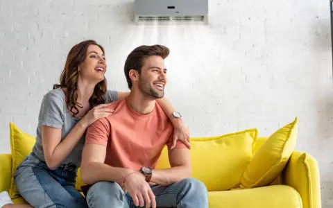 Couple souriant sur un canapé jaune, profitant de la brise fraîche d'un climatiseur moins de 50 db.