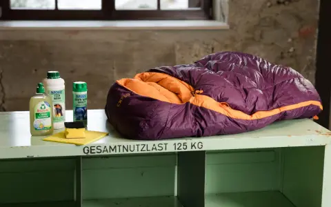 Lila-orangefarbener Exped-Schlafsack bereit zum Schlafsack waschen, daneben Reinigungsmittel und Schwamm.