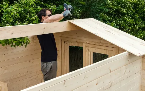 Hombre ensamblando una caseta de jardín con maderas para exterior.