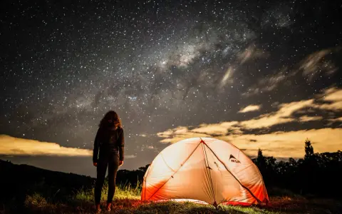Nuit étoilée sur un bivouac GR34. Une personne admire la Voie lactée près d'une tente illuminée.