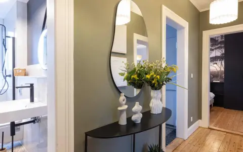 Élégant couloir maison avec miroir asymétrique, vases décoratifs, bouquet de fleurs jaunes et vue sur une salle de bain et une chambre.