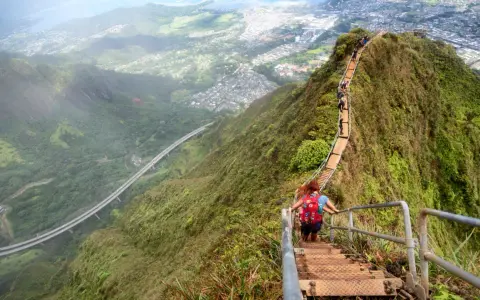 Wanderer erklimmen die "Stairway to Heaven" in Hawaii, eine steile Treppe mit atemberaubendem Blick auf die Stadt und die Natur.