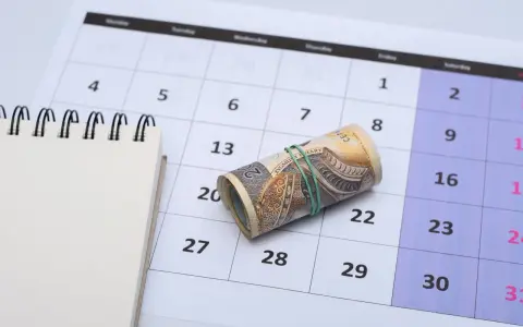 Zrolowane banknoty na kalendarzu, symbolizujące ekwiwalent czasu i pieniędzy. Obok pusty notatnik.