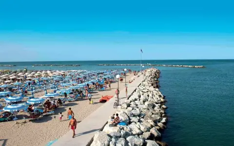 Spiaggia affollata a Gatteo Mare Cesenatico, con ombrelloni, lettini e persone che passeggiano sul molo.