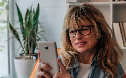 Kobieta w okularach przegląda telefon, być może szuka bratniej duszy na **Bumble w Polsce**.