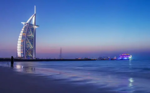Wieczór w Dubaju. Luksusowy hotel Burdż al-Arab i oświetlony statek na morzu. Ceny w Dubaju mogą być wysokie, ale widoki są niezapomniane.