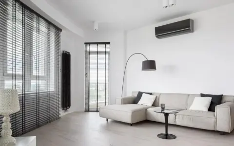 Unità interna di climatizzatore su parete bianca, con divano e lampada. Ideale per capire la differenza tra monosplit e dualsplit.