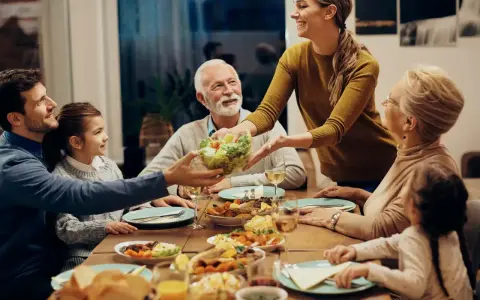 Une famille partage un repas joyeux. La mère sert la salade, et tout le monde sourit. C'est un moment de partage, alors pourquoi ne pas mettre les coudes sur la table ?