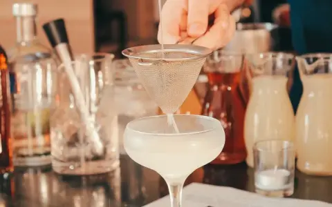 Ile napojów na wesele 80 osób? Barman przygotowuje drinka, w tle butelki z alkoholami i syropami.
