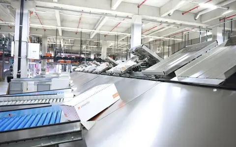 Nowoczesna sortownia paczek z taśmociągami. Jedna z paczek z logo Zalando przesuwa się po pochylni, gotowa do dalszej podróży.