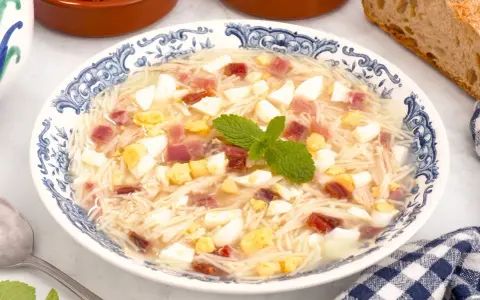 Sopa de picadillo andaluza en un plato azul y blanco con trocitos de huevo duro, jamón y fideos finos.