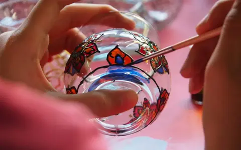Manos pintando un vaso de cristal con flores de colores. Aprende como pintar cristal a mano y crea arte.