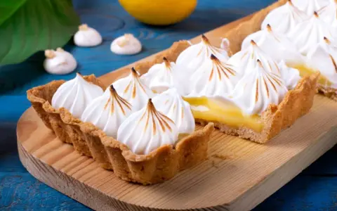 Tarta de limón con abundante merengue suizo tostado, sobre una tabla de madera.