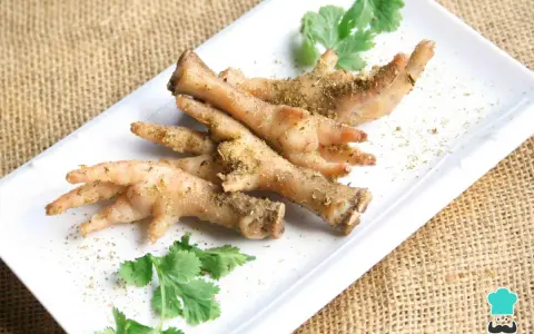Patas de pollo sazonadas y listas para cocinar, adornadas con cilantro fresco sobre un plato blanco.