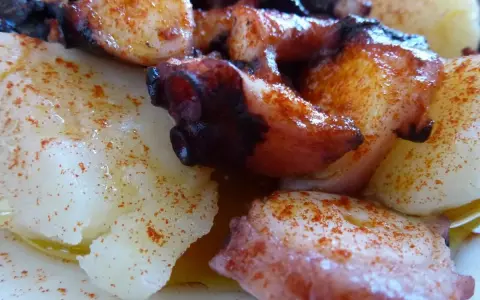 Pulpo con cachelos, un plato gallego tradicional. Tentáculos de pulpo cocidos y trozos de patata, todo espolvoreado con pimentón y aceite de oliva.