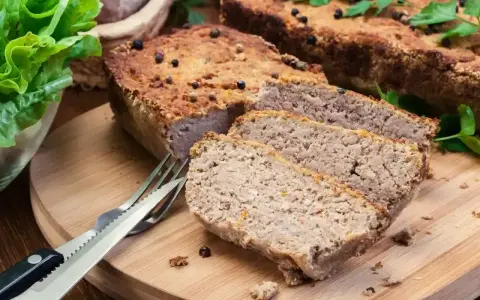 Domowy pasztet, idealny do pieczenia w temperaturze 180°C, pokrojony na desce z widelcem i sałatą.