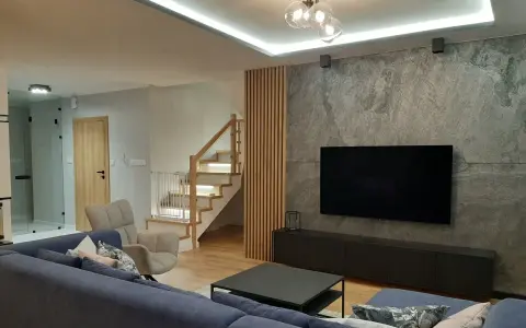 Nowoczesny salon z szarą ścianą, telewizorem i drewnianymi lamelami. Zobacz, z czym łączyć lamele, by stworzyć przytulne wnętrze.