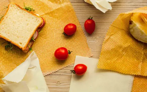 Un sandwich, des tomates et un morceau de fromage sont présentés sur des bee wraps maison à pois rouges sur fond de bois.