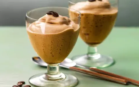 Due bicchieri di spumone al caffè, guarniti con chicchi di caffè, su un tavolo verde.