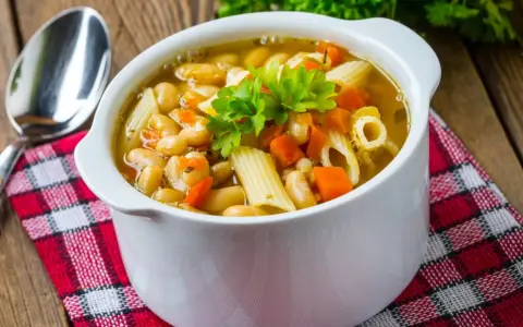 Pyszna zupa z makaronem, fasolą i marchewką, udekorowana natką pietruszki. Idealna na chłodne dni.
