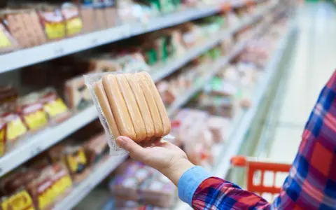 Ręka trzyma paczkę parówek w supermarkecie. Zastanawiasz się, ile kalorii ma parówka?