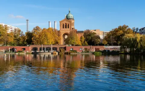 Herbstliche Bäume spiegeln sich im Wasser des Engelbeckens Berlin. Ein Café mit Außenbereich und eine Kirche mit Kuppel sind zu sehen.