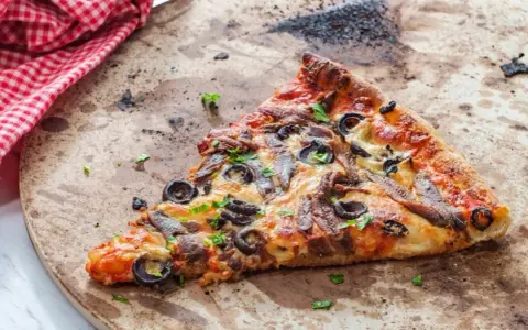 Une part de pizza aux anchois et olives sur une pierre réfractaire, prête pour un nettoyage.