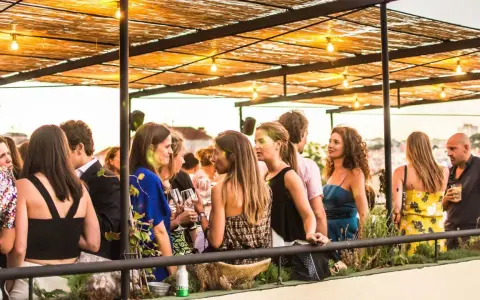Menschen genießen den Abend auf einer Dachterrasse in einem **bar lissabon**. Unter einem Strohdach mit Lichterketten unterhalten sie sich bei Getränken.