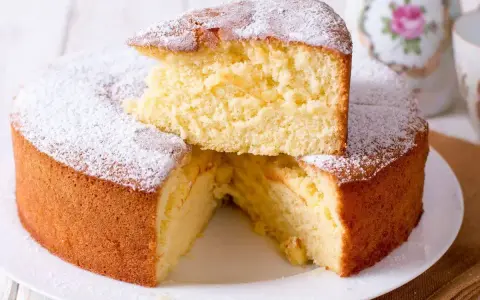 Una soffice torta fredda allo yogurt, spolverata di zucchero a velo, con una fetta sollevata che ne rivela la morbidezza.