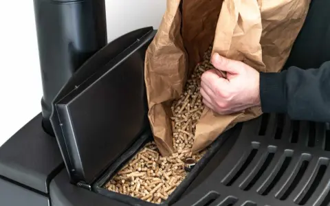 Persona rellena un compartimento de estufa de pellets. Considera el instalar estufa pellets precio para un hogar eficiente.