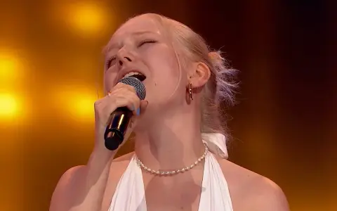 Paulina Pytlak śpiewa z pasją, z zamkniętymi oczami i mikrofonem w dłoni, na tle złocistych świateł.