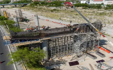 Obreros trabajan en la construcción de puentes de acero, con grúas y andamios rodeando las estructuras.