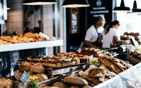 Stoisko z pieczywem i ciastami, przypominające najtańsze supermarkety we Włoszech. W tle widać sprzedawców.
