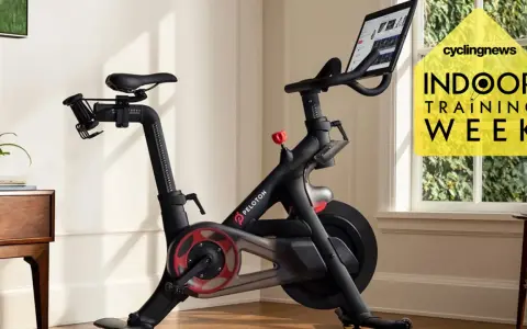 A Peloton bike, perfect for indoor cycling vs spinning, sits in a bright room. A yellow graphic promotes "Indoor Training Week.