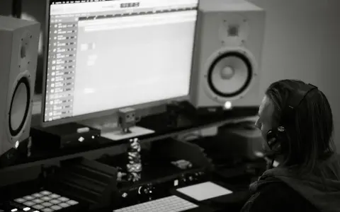 Producent muzyczny w słuchawkach tworzy beaty w studiu. Zastanawia się, czym się różni trap od rapu, analizując dźwięki na monitorze.