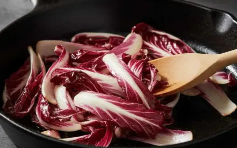 Fette di radicchio rosso vengono saltate in padella con un cucchiaio di legno.